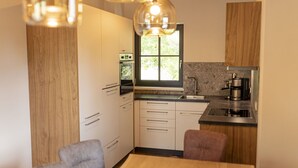 Una cucina moderna con mobili in legno, forno integrato, lavello e macchina per il caffè. Sopra il lavello c'è una finestra e un tavolo da pranzo con sedie.