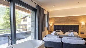 Una camera da letto moderna con una grande vasca da bagno, un letto matrimoniale con asciugamani ordinatamente piegati e vista su un paesaggio montano attraverso ampie finestre.