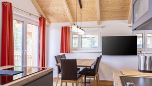 Una cucina moderna con travi in legno, un'area pranzo con sedie e un grande televisore a parete.