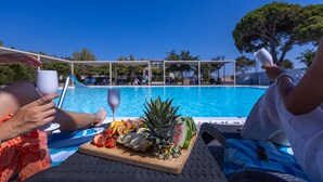 A poolside setting with a wooden board holding fruits and a glass, and a person holding a glass. - Buka Sandy Beach  (Messini)