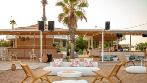 A beachside lounge with a white sofa set, wicker chairs, and a bar area with patrons. - Buka Sandy Beach  (Messini)