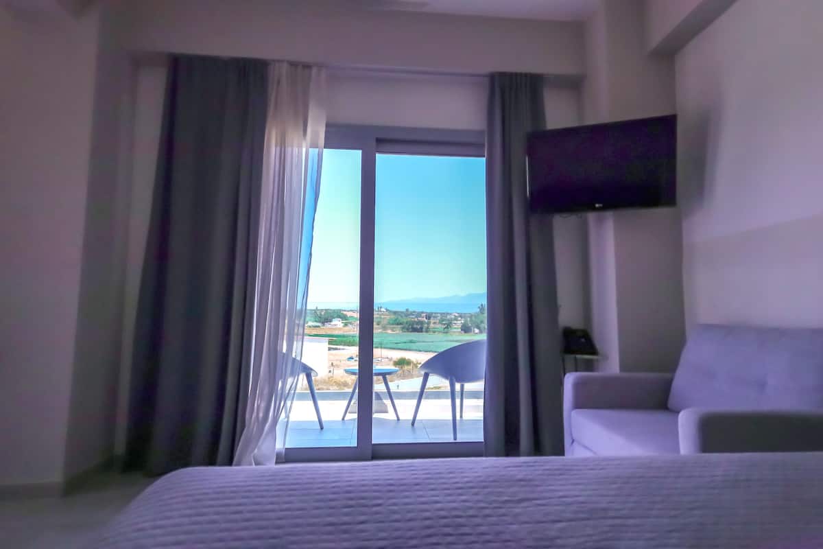 A hotel room with a bed, a TV mounted on the wall, and a view of the countryside through a large window.