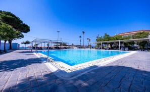 A swimming pool with a tiled deck, surrounded by umbrellas and lounge chairs.