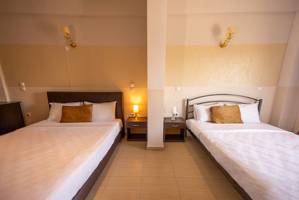 A hotel room with two single beds, each with a nightstand, a lamp, and a wall-mounted light fixture.
