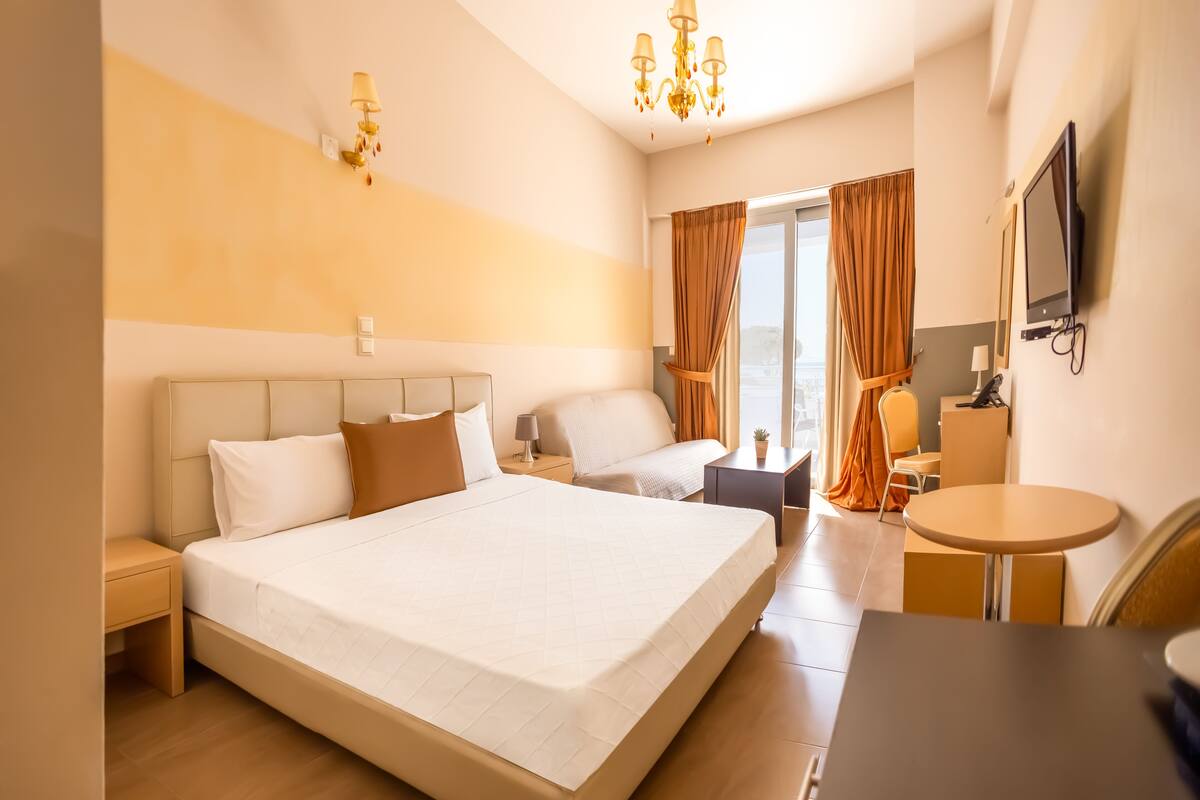 A hotel room with a large bed, a desk, a chair, a TV, and a window with curtains.