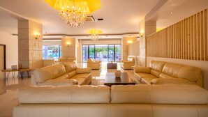 A spacious living area with leather sofas, a chandelier, and a view of the outdoors. - Buka Sandy Beach  (Messini)