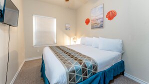 Un dormitorio con cama, ventilador de techo, televisor montado en la pared y ventana con persianas.