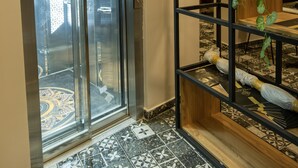 Um elevador com visor digital, piso estampado e prateleira de madeira com plantas.