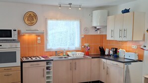 A kitchen with a microwave, oven, sink, and cabinets. There is a window with a curtain, a clock, and a decorative plate on the wall.