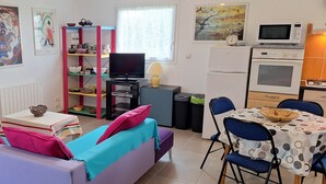 A cozy living room with a sofa, a television, a small table, and a kitchen area with a microwave and oven.