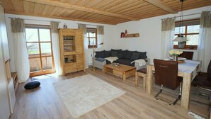 A cozy living room with a sofa, coffee table, and a dining area with a table and chairs. There is a wooden cabinet with glassware and a floor lamp.