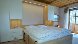 A modern bedroom with a wooden bed, built-in storage, and a large window with a view.