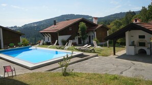 A pool area with lounge chairs, a small pool, and a building with a chimney.