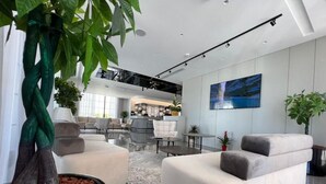Una sala de estar moderna con un sofá grande, una mesa de centro y una planta en maceta. Se aprecia un comedor al fondo, con techo alto y una escalera.