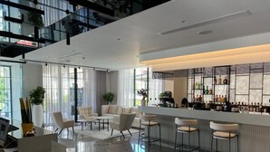 Un vestíbulo de hotel moderno con una zona de bar, asientos y una recepción.