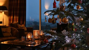 Una sala de estar acogedora con un árbol de Navidad, una lámpara y vistas de la ciudad al anochecer.