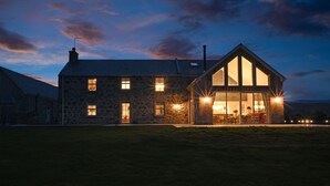 Una casa de piedra con un amplio ventanal de vidrio, múltiples ventanas y un interior luminoso.