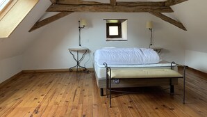 A bedroom with a wooden floor, a bed with a mattress and pillows, two bedside tables with lamps, a small window, and exposed wooden beams on the ceiling. - Charmante Maison Périgourdine (Granges-d'Ans)