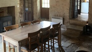 A rustic stone interior with a wooden dining table and chairs, a stone fireplace, and a window allowing natural light. - Charmante Maison Périgourdine (Granges-d'Ans)
