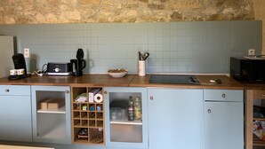 A kitchen with a stone wall, a coffee maker, a bowl of cereal, and a microwave. - Charmante Maison Périgourdine (Granges-d'Ans)