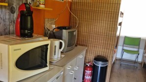 Eine kompakte Küche mit einer Mikrowelle, einem Wasserkocher und einer Kaffeemaschine auf der Arbeitsplatte, einem kleinen Kühlschrank und einem Mülleimer.