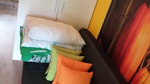 Ein schwarzes Sofa mit vielen Kissen in verschiedenen Farben, eine weiße Kommode mit zwei Griffen und ein Gemälde von roten und orangen Blumen an der Wand.