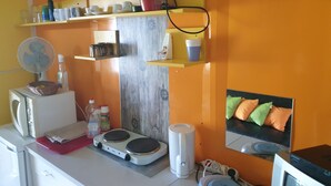 Eine Küche mit Mikrowelle, Wasserkocher und Kaffeemaschine. Regale mit Tassen und ein Korb sind ebenfalls vorhanden.