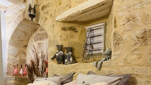 Un dormitorio acogedor con pared de piedra, cama con ropa de cama estampada y elementos decorativos, incluyendo peluches y cuadros.