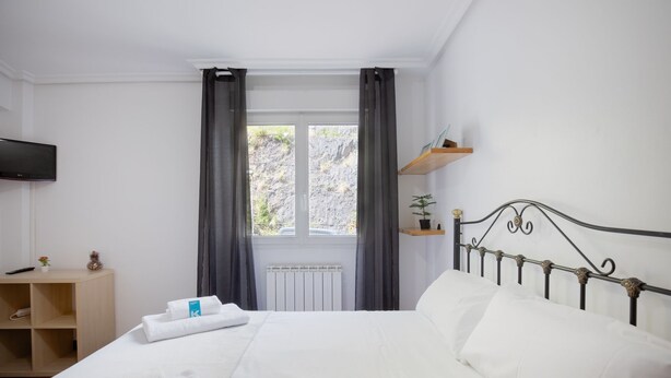 Una habitación de hotel con cama, televisión, escritorio y ventana con cortinas.