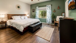A bedroom with a wooden bed, a ceiling fan, a window with curtains, a nightstand, a dresser, and a refrigerator. - Modern, 3 Bedroom Home Near Superstition Mountain! (Apache Junction)