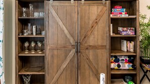 A wooden cabinet with sliding doors, shelves with glassware, and storage boxes. - Modern, 3 Bedroom Home Near Superstition Mountain! (Apache Junction)