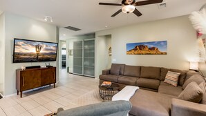 A living room with a large flat-screen TV, a brown sofa, a gray armchair, and a small coffee table. - Modern, 3 Bedroom Home Near Superstition Mountain! (Apache Junction)