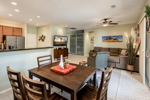 A modern kitchen with wooden cabinets, a dining table with chairs, a TV, and a sofa in a living area.