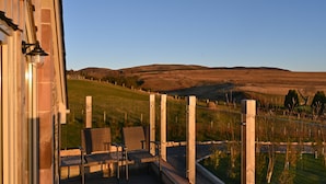 A balcony with wicker chairs and a view of a grassy field and hills. - Luxury two bedroom converted steading (Perth)