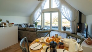 A dining area with a table set for breakfast, including croissants, coffee, and juice. There is a sofa and a television in the background. - Luxury two bedroom converted steading (Perth)