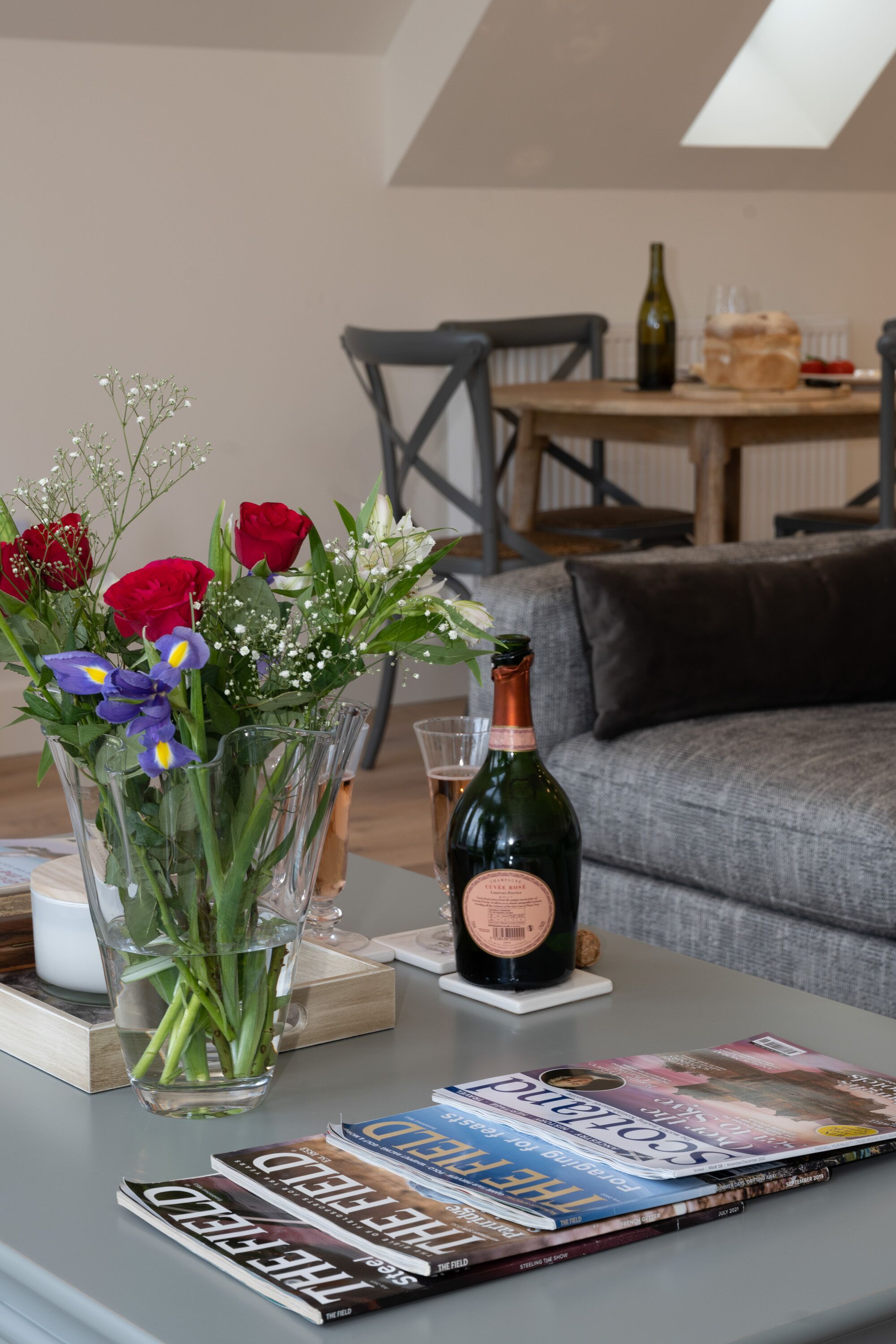 A living room with a coffee table holding a vase of flowers, a bottle of wine, and a magazine.