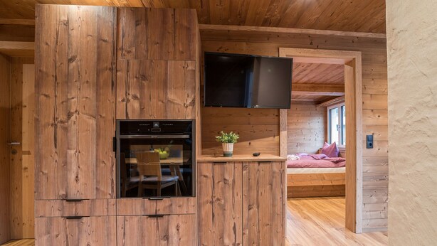 A wooden interior with a built-in kitchen, a flat-screen TV, and a cozy seating area. - 1213 Vallüla Schima Drosa (Gaschurn)