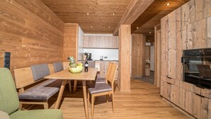 A wooden interior with a dining table, chairs, and a kitchen area. - 1213 Vallüla Schima Drosa (Gaschurn)
