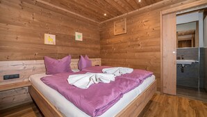 A wooden-paneled bedroom with a bed, pillows, and a bathroom visible through an open door. - 1214 Piz Buin Schima Drosa (Gaschurn)