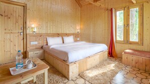 A wooden room with a bed, a table with a bottle and glasses, and a bench.