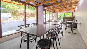 A covered outdoor dining area with tables and chairs, large windows, and a view of the street.