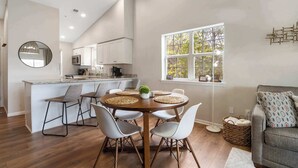 A modern kitchen with white cabinets, a round dining table with four chairs, and a large window providing natural light. - Whiskey's Hillside Retreat -holiday Hills Branson - Golf Resort (Branson)