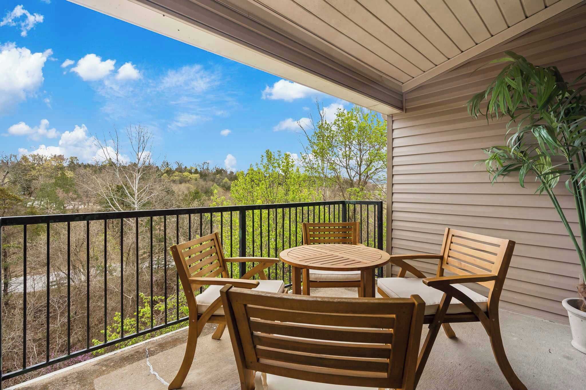 Un balcon avec une table ronde et quatre chaises en bois, un pot de fleurs et une vue sur un paysage vallonné.