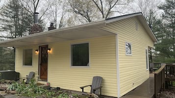 Enjoy a peaceful stay in this cozy cabin with a covered porch and two windows, surrounded by a deck and stone wall.