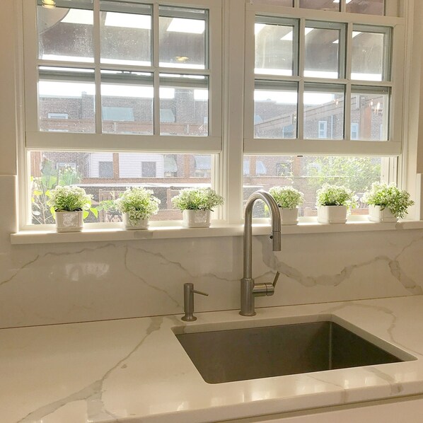 A kitchen with a white marble countertop, a sink, and a window with multiple panes.
