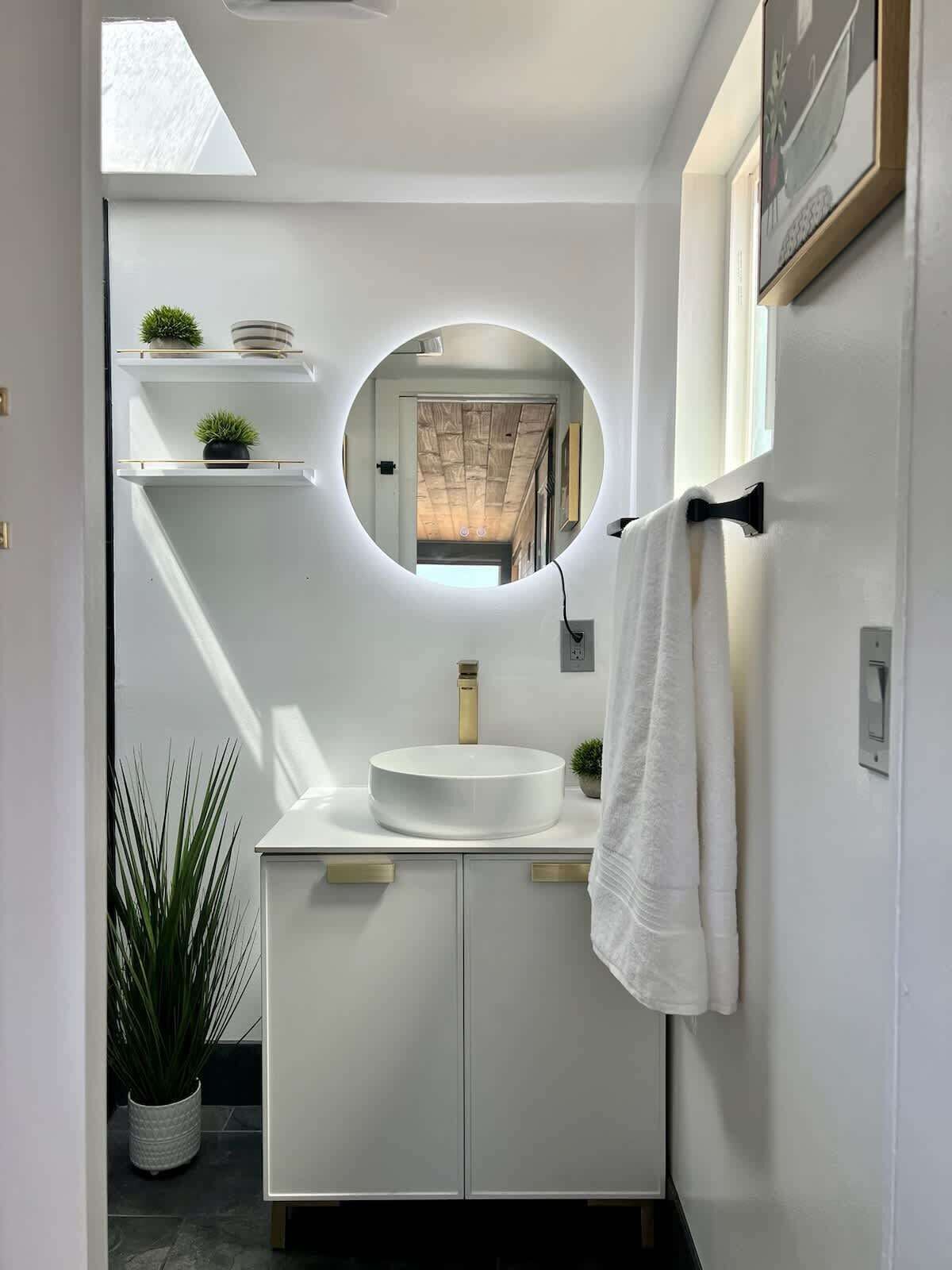 Une salle de bain moderne avec un miroir rond, un meuble-lavabo blanc et un porte-serviettes.