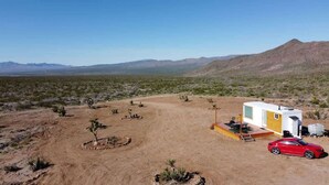 Un paysage désertique avec un petit bâtiment d’un seul étage, doté d’un patio et d’une voiture rouge garée à proximité.
