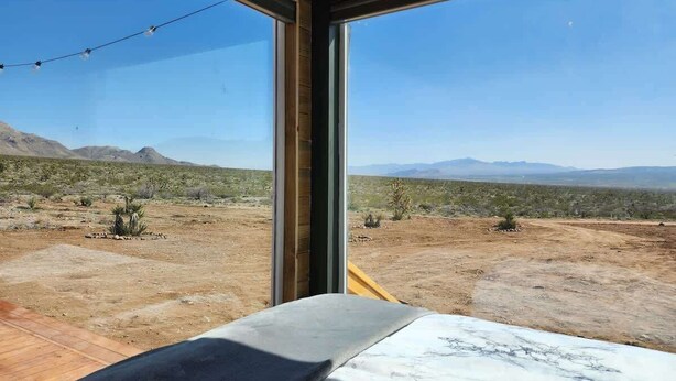 Une pièce dotée d’une grande fenêtre donnant sur un paysage désertique, avec des montagnes à l’horizon.