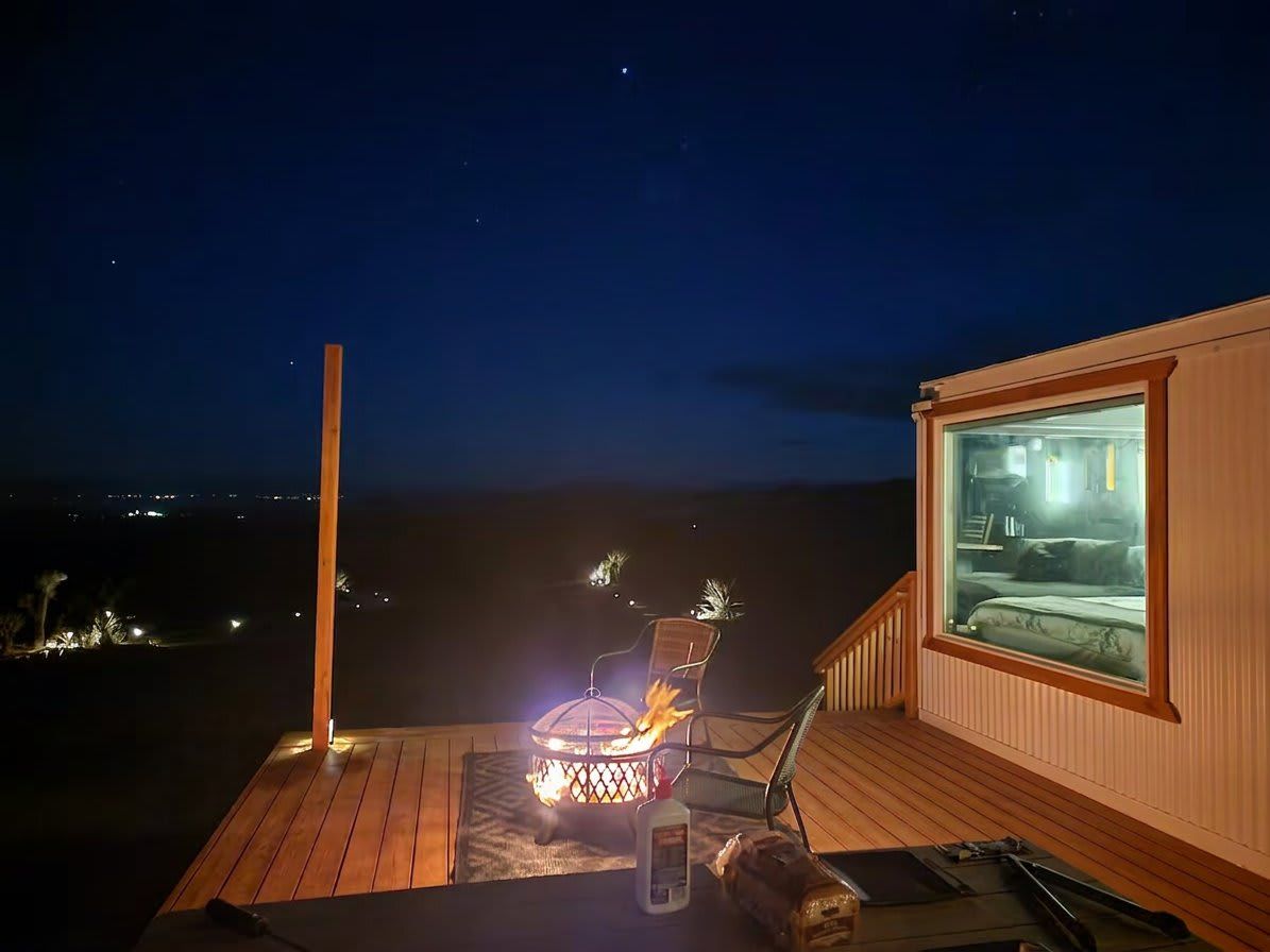 Een terras met een vuurplaats, een stoel en uitzicht op een slaapkamer door een raam.