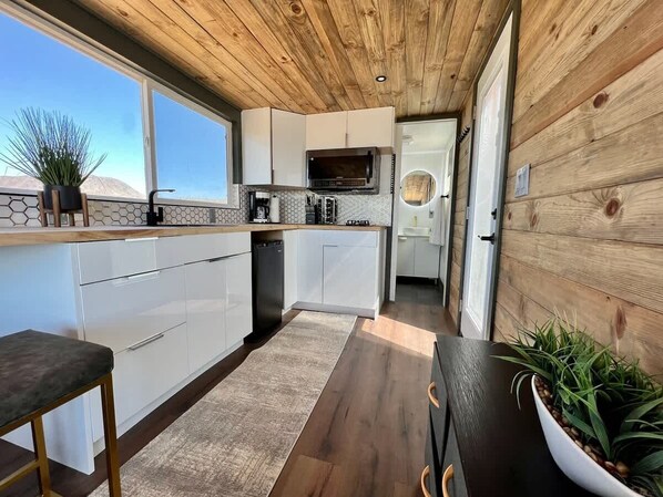 Eine moderne Küche mit weißen Schränken, einer Holzbalkendecke und Blick ins Freie.